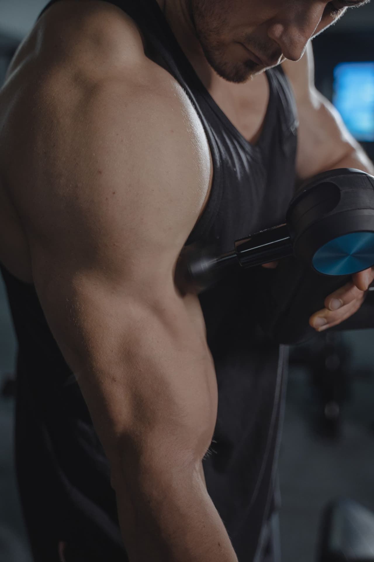 A handheld percussion massage device being applied to a patient's shoulder muscle