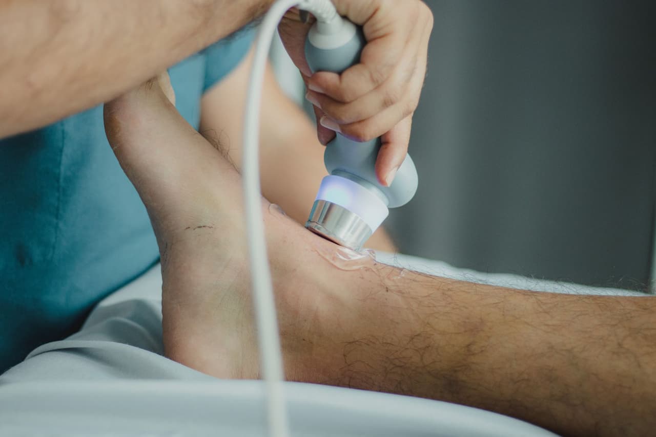 A clinician moving a therapeutic ultrasound wand over gel on a patient's shoulder